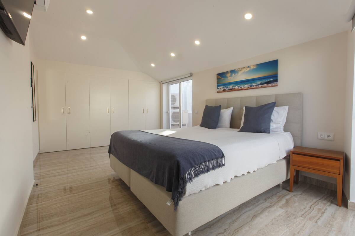 A bedroom with a bed, a nightstand, a painting, and a wardrobe.