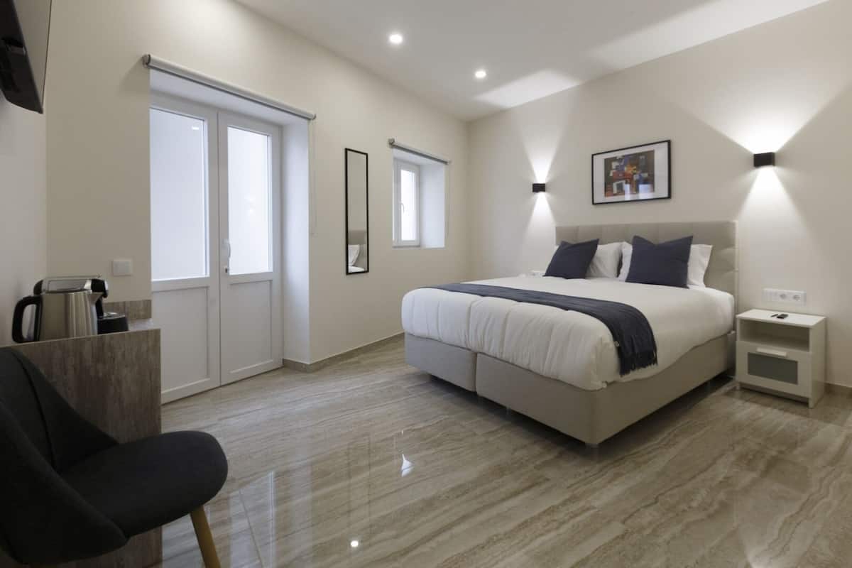 A modern bedroom with a large bed, bedside tables, a chair, and a coffee maker.
