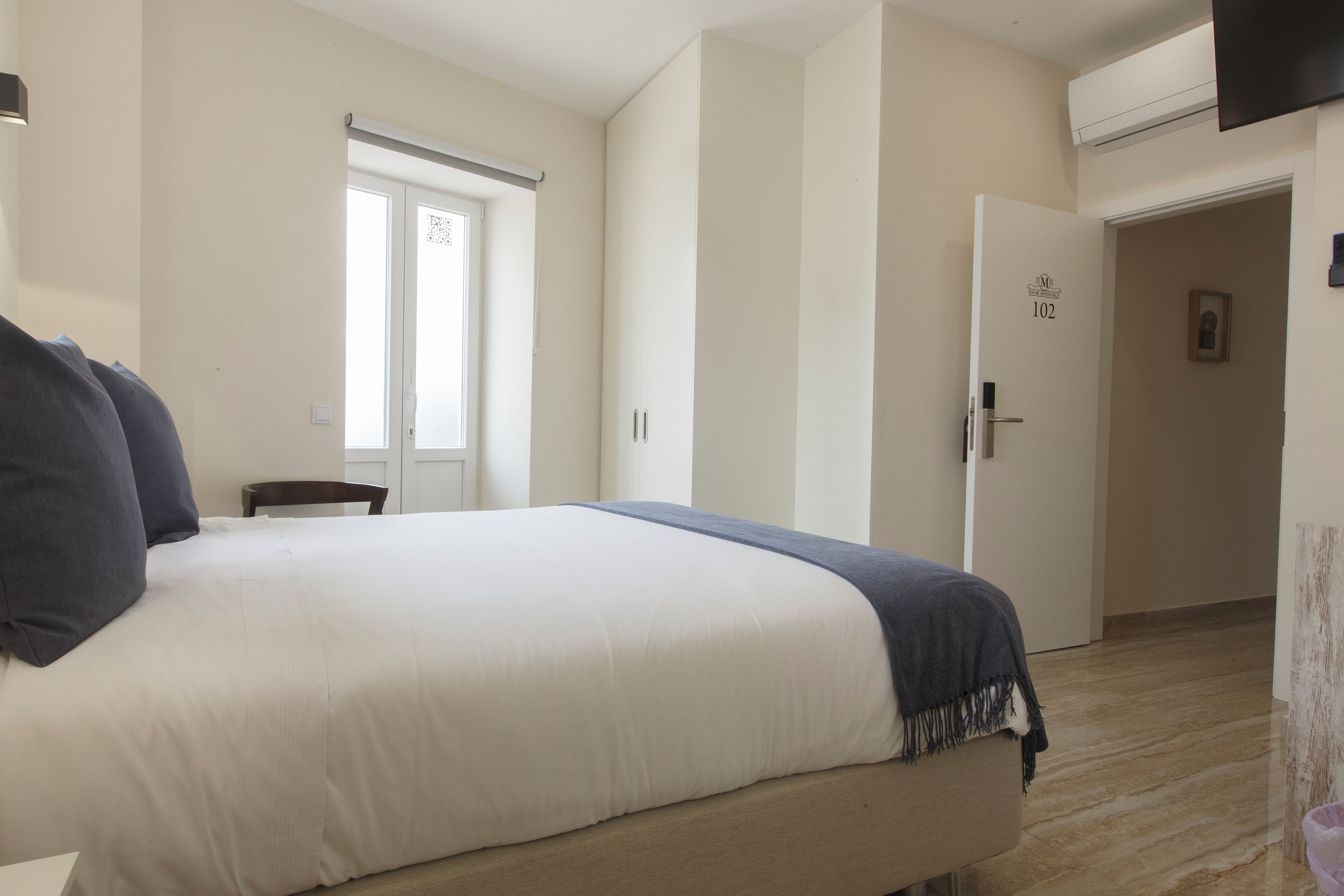 Ein Schlafzimmer mit einem Bett, einem Sessel, einer Tür und einem an der Wand montierten Fernseher.