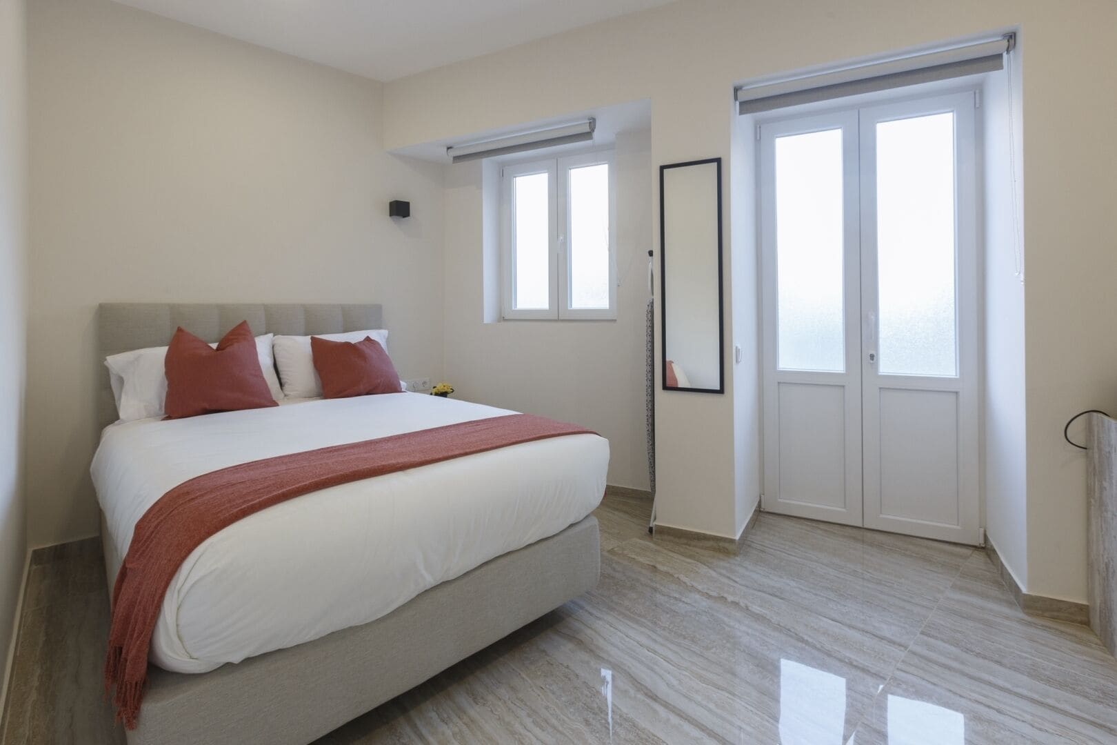 Un dormitorio con cama, ventana, puerta y espejo.