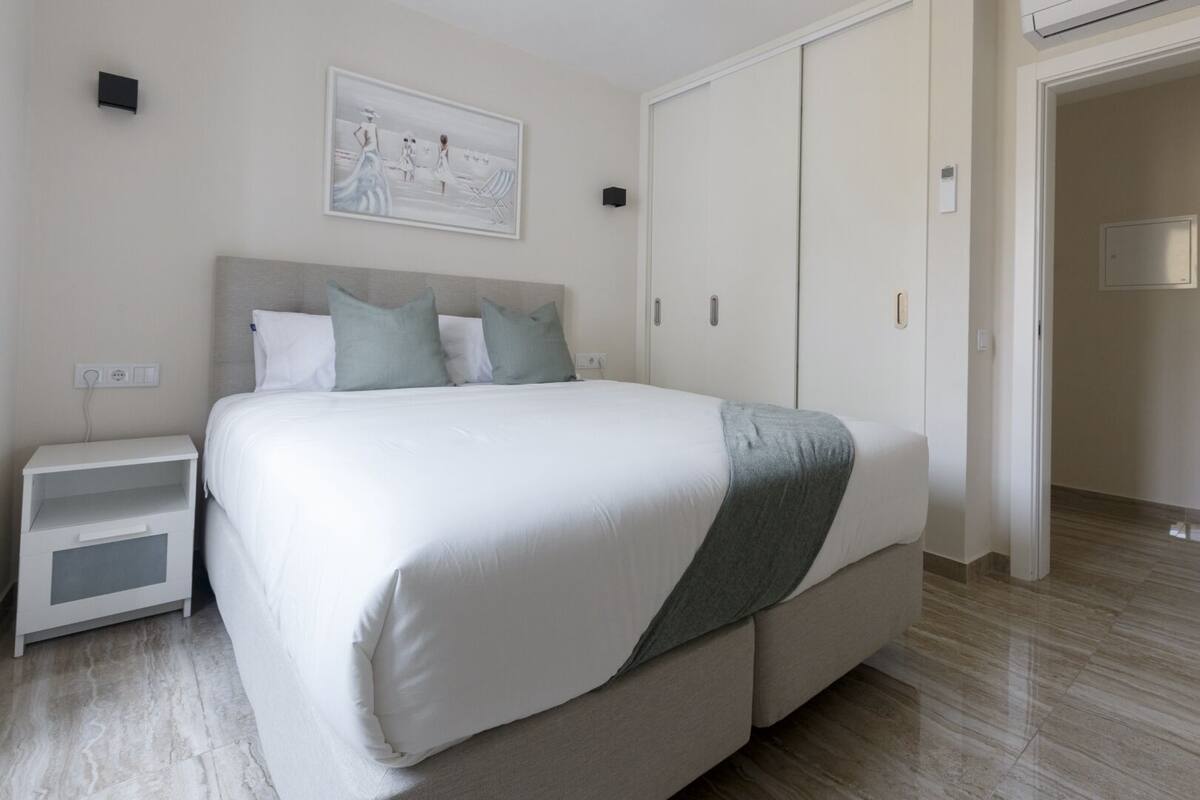 A modern bedroom with a large bed, a nightstand, a wardrobe, and a painting on the wall.