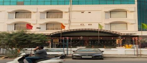 Un hotel con fachada moderna, un acceso cubierto y una bandera al frente.