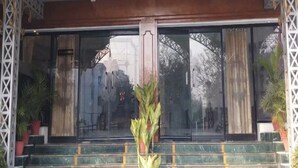 A hotel entrance with a large glass door, a wooden arch, and steps leading up to it. - Hotel Ajay International (Prayagraj)