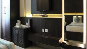 A modern hotel room with a flat-screen TV mounted on a dark wall, a bedside table with a lamp, and a large mirror reflecting the room. - Hotel Ajay International (Prayagraj)