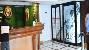 A reception area with a green wall, a reception desk, and a glass door leading to a hallway. - Hotel Ajay International (Prayagraj)