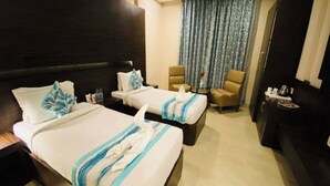 A hotel room with two beds, a sofa, a chair, and a small table. - Hotel Ajay International (Prayagraj)
