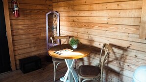 Interior de una cabaña de madera con una mesa redonda, dos sillas, una planta pequeña en maceta, un extintor y un microondas.