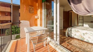 Ein Balkon mit Tisch und Stühlen, ein Bett mit Blumenmuster-Bettwäsche und Blick auf die Straße.