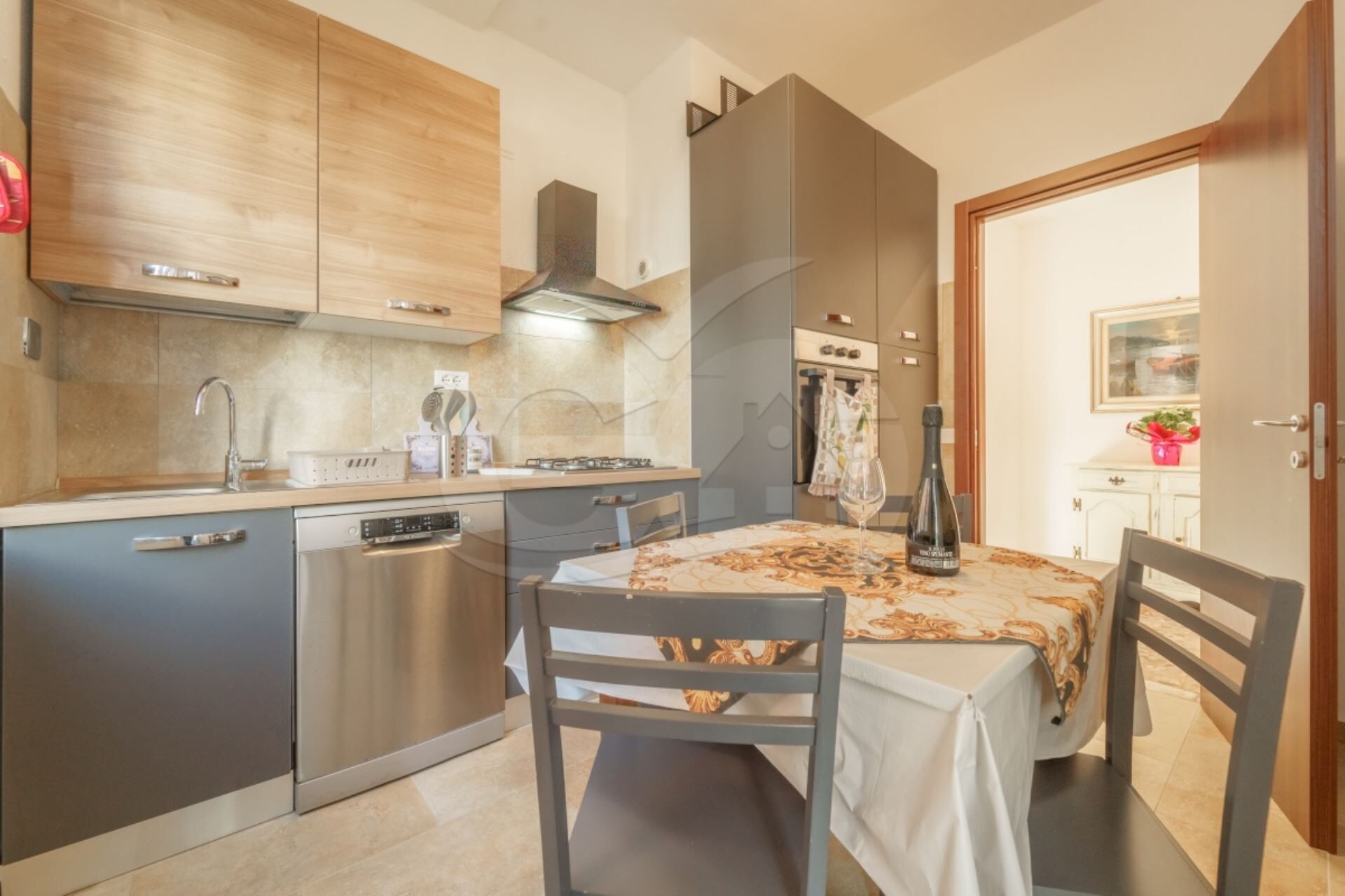 Et kompakt køkken med moderne hårde hvidevarer, et spiseområde med et bord dækket til to, og udsigt til den tilstødende opholdsstue.