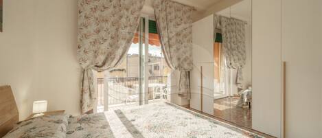 A bedroom with a bed, a mirror, and a view of the outside balcony.