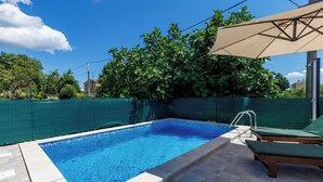 A swimming pool with a tiled deck, a lounge area with a canopy, and a green fence surrounding the area. - House Papinka With Private Pool & Garden (Sveta Nedelja)