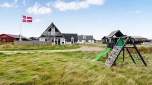 A playground with a green slide and climbing net, set against a backdrop of houses with a flagpole. - "Kaja" - 150m from the sea by Interhome (Harboøre)