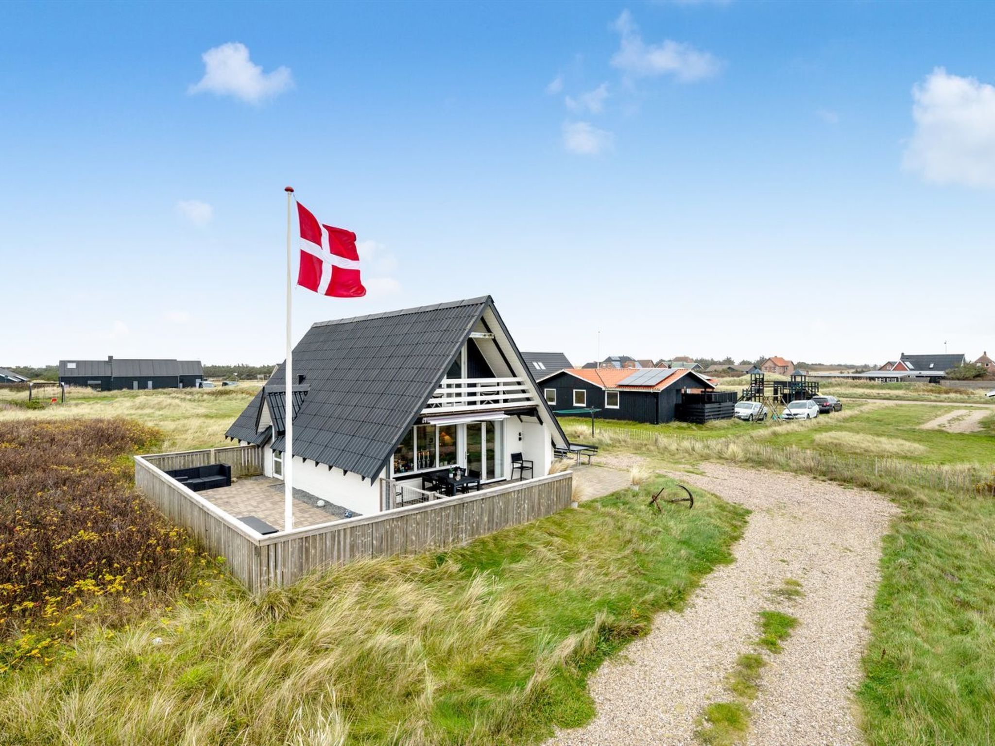 A coastal house with a flag, a deck, and a gravel path.