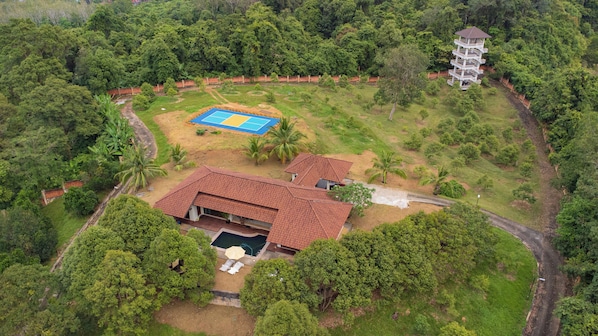 An aerial view of a property with a large house, a tennis court, and a multi-story building.