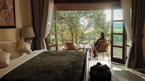 Een slaapkamer met een bed, nachtkastje, lamp, raam en uitzicht op de omgeving.