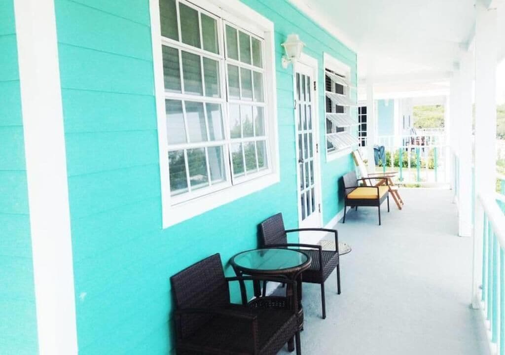 A turquoise building with white trim, a covered porch with wicker furniture, and a view of the surrounding area.
