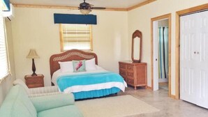 A bedroom with a bed, a nightstand, a dresser, a mirror, and a door. - Exuma Beach Point (Rolleville)