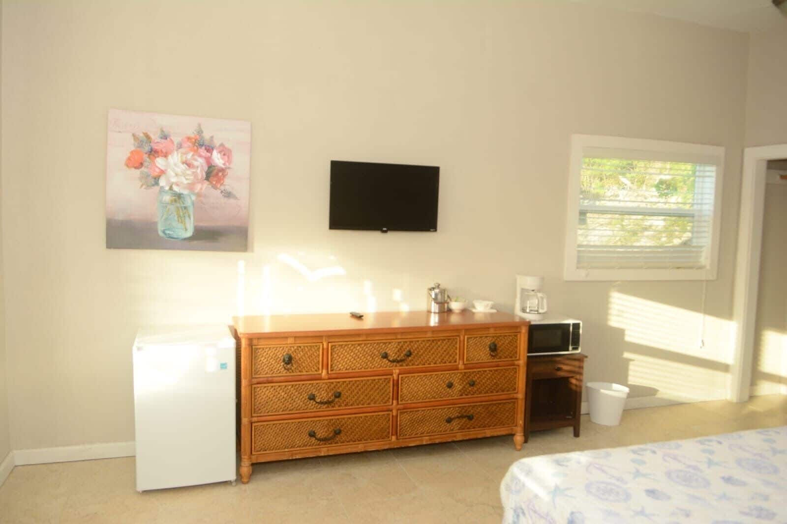 Un dormitorio con un aparador de madera, un televisor de pantalla plana, un refrigerador y una ventana con persianas.