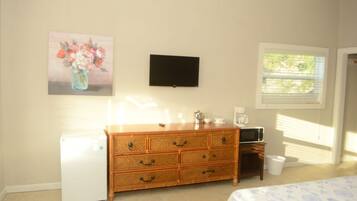 Un dormitorio con un aparador de madera, un televisor de pantalla plana, un refrigerador y una ventana con persianas.