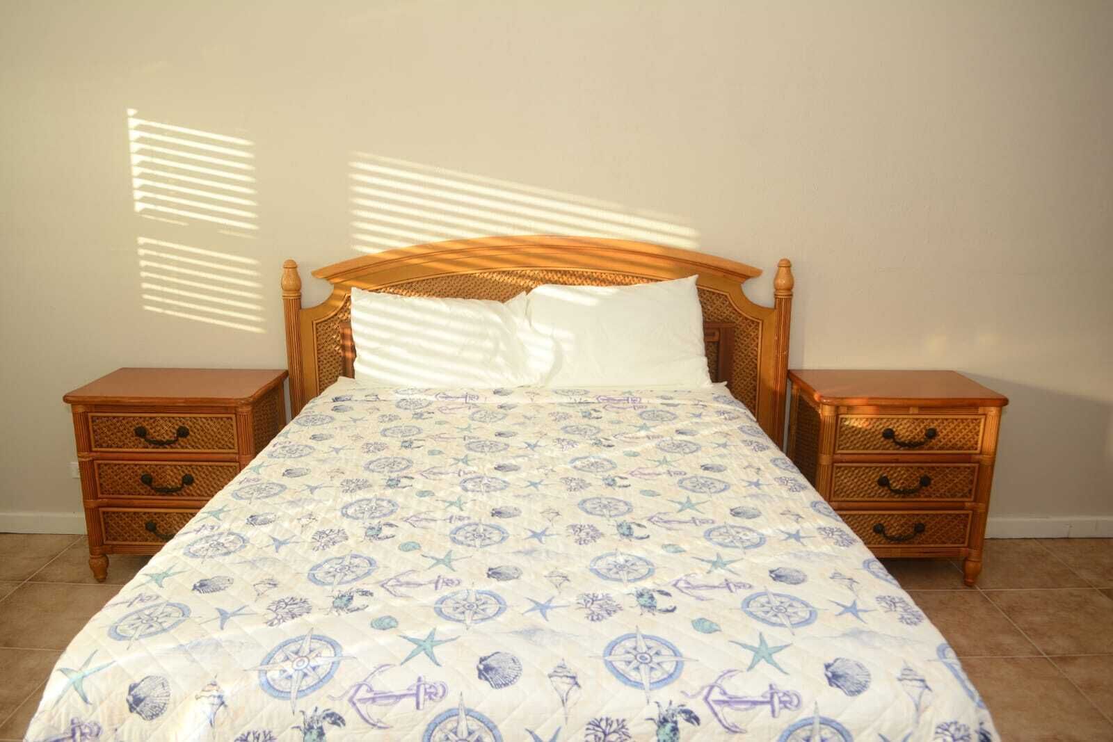 Un lit recouvert d’une couvre-lit à motifs, deux tables de chevet en bois et un mur uni.