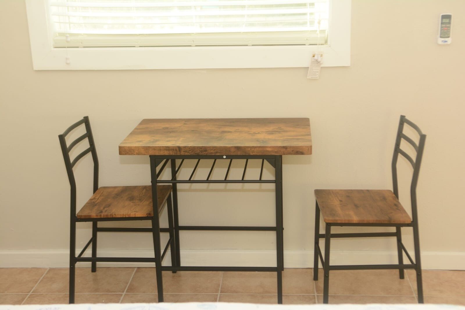 A small dining table with two chairs, a window with blinds, and a wall-mounted phone.