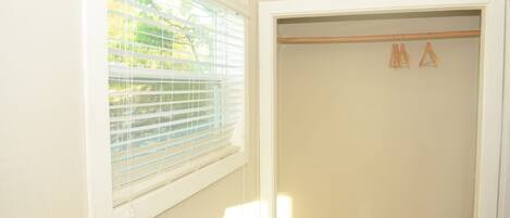 Una habitación con ventana, un armario de madera con perchas y una puerta blanca.