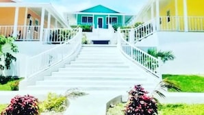 A staircase leading to a house with a green roof, surrounded by white railings and greenery. - Exuma Beach Point (Rolleville)