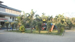 A playground with slides and climbing structures, surrounded by palm trees and a building with a sign that reads "Satyadri Rooms". - Sahyadri Guest House (Talasri)