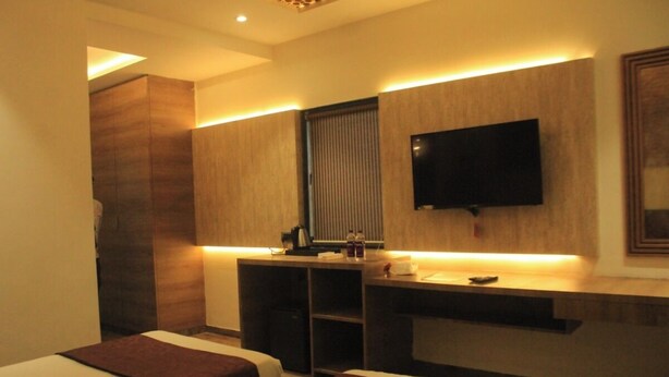 A hotel room with two beds, a desk with a flat-screen TV, and a mirror on the wall. - Sahyadri Guest House (Talasri)