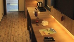 A modern hotel room with a wooden floor, a flat-screen TV mounted on the wall, a small table with a kettle, a bottle of water, and a remote control. - Sahyadri Guest House (Talasri)