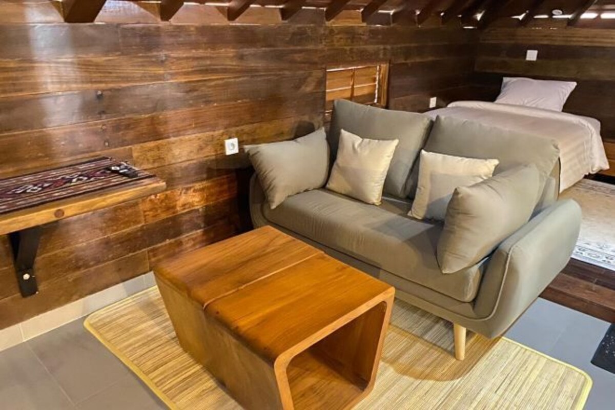 A cozy room with a wooden ceiling, a sofa, a small wooden table, and a bed with a headboard.