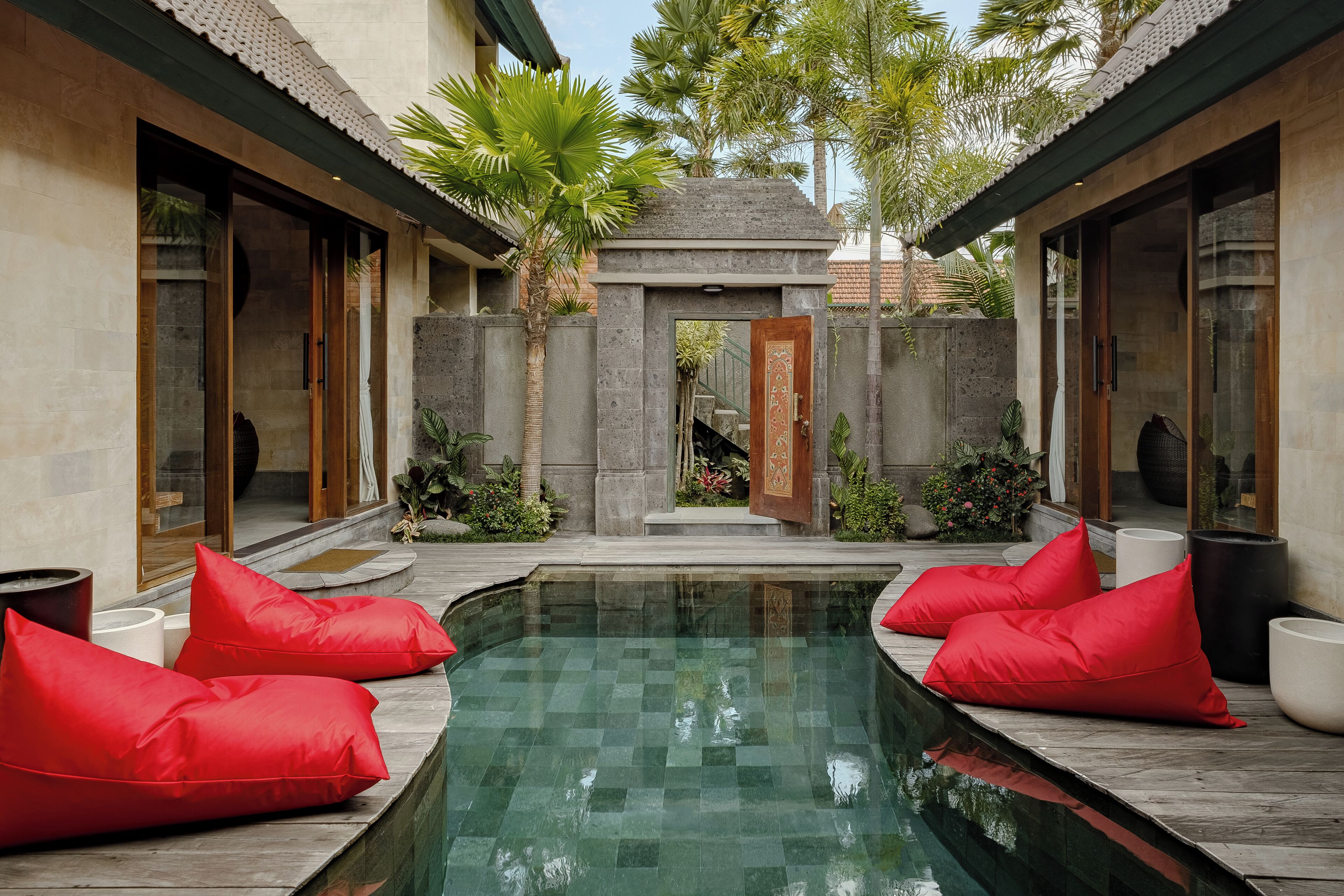A serene pool area with red cushions, a stone pathway, and lush greenery.
