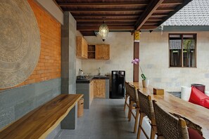 A kitchen with a wooden bench, a dining table with chairs, a refrigerator, and a hanging light fixture. - Monique Ubud Villa (Ubud)