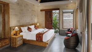 A spacious bedroom with a large bed, a wooden headboard, a nightstand, and a wicker chair. - Monique Ubud Villa (Ubud)