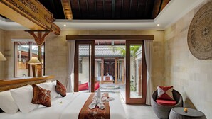 A hotel room with a large bed, a sitting area with wicker furniture, and a view of a traditional courtyard. - Monique Ubud Villa (Ubud)