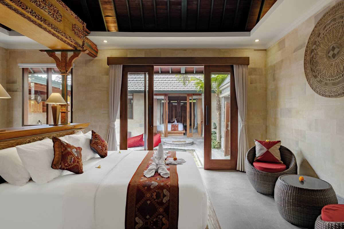 A hotel room with a large bed, a sitting area with wicker furniture, and a view of a traditional courtyard.