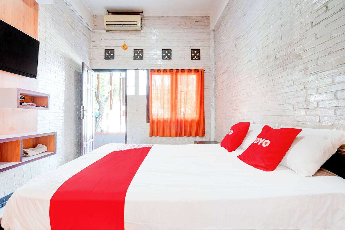 Een hotelkamer met een groot bed, witte en rode beddengoed, een aan de muur gemonteerde televisie en een bakstenen muur.