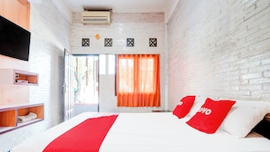 Een hotelkamer met een groot bed, witte en rode beddengoed, een aan de muur gemonteerde televisie en een bakstenen muur.