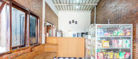 A narrow hallway with a checkered floor, wooden benches, a brick wall, and a refrigerated display case with snacks.