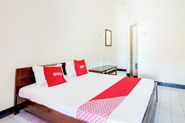 A neatly made bed with a white and red bedspread, two red pillows with "OYO" branding, and a wooden headboard.