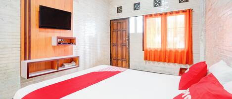 A hotel room with a bed, a TV mounted on the wall, a window with curtains, and a wooden door.