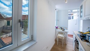 Una cuina moderna amb armaris blancs, una taula de dinar i vista a la ciutat a través de grans finestres.