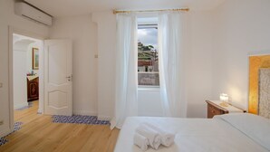 Una habitació d'hotel amb un llit, una petita taula de nit, una finestra amb cortines i vista a un edifici.