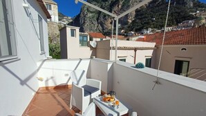 Un balcó amb moble de vimet trenat blanc, una taula amb articles per esmorzar i vista a un paisatge de muntanya.