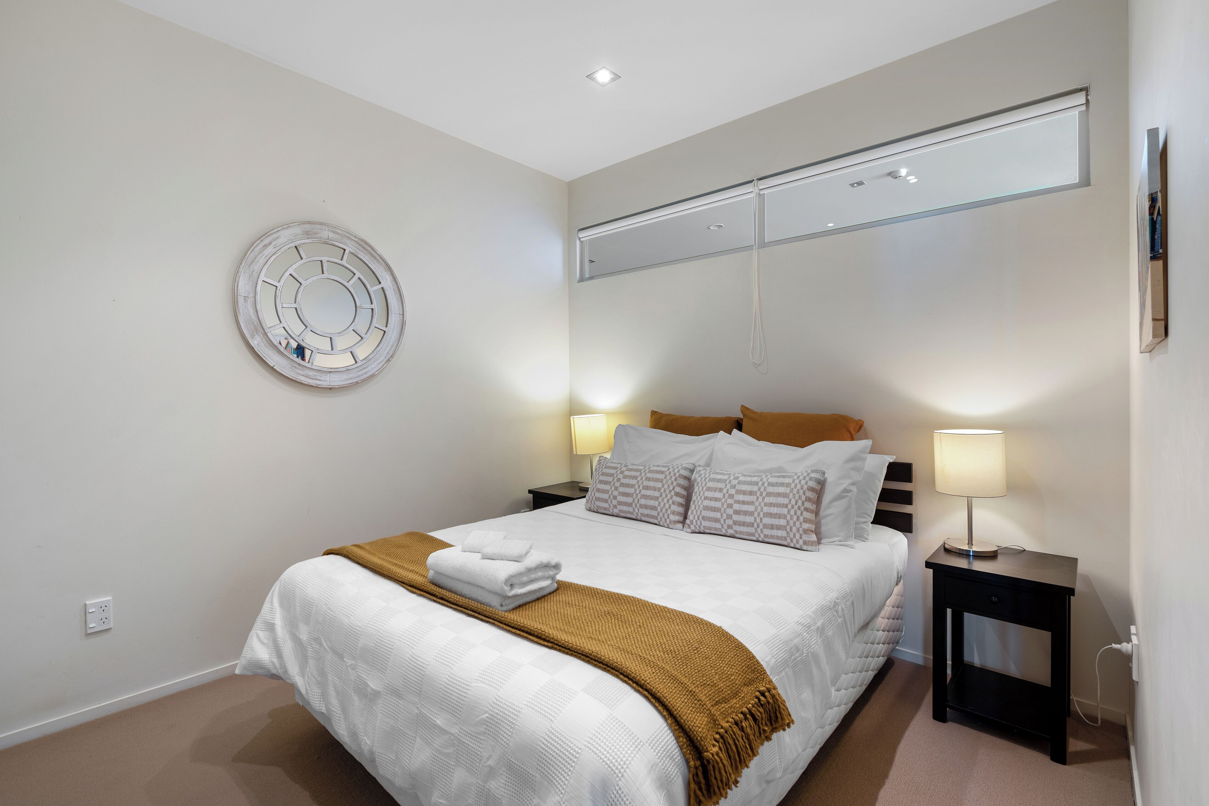 A neatly arranged bedroom with a bed, bedside tables, a wall-mounted light, and a circular wall decoration.