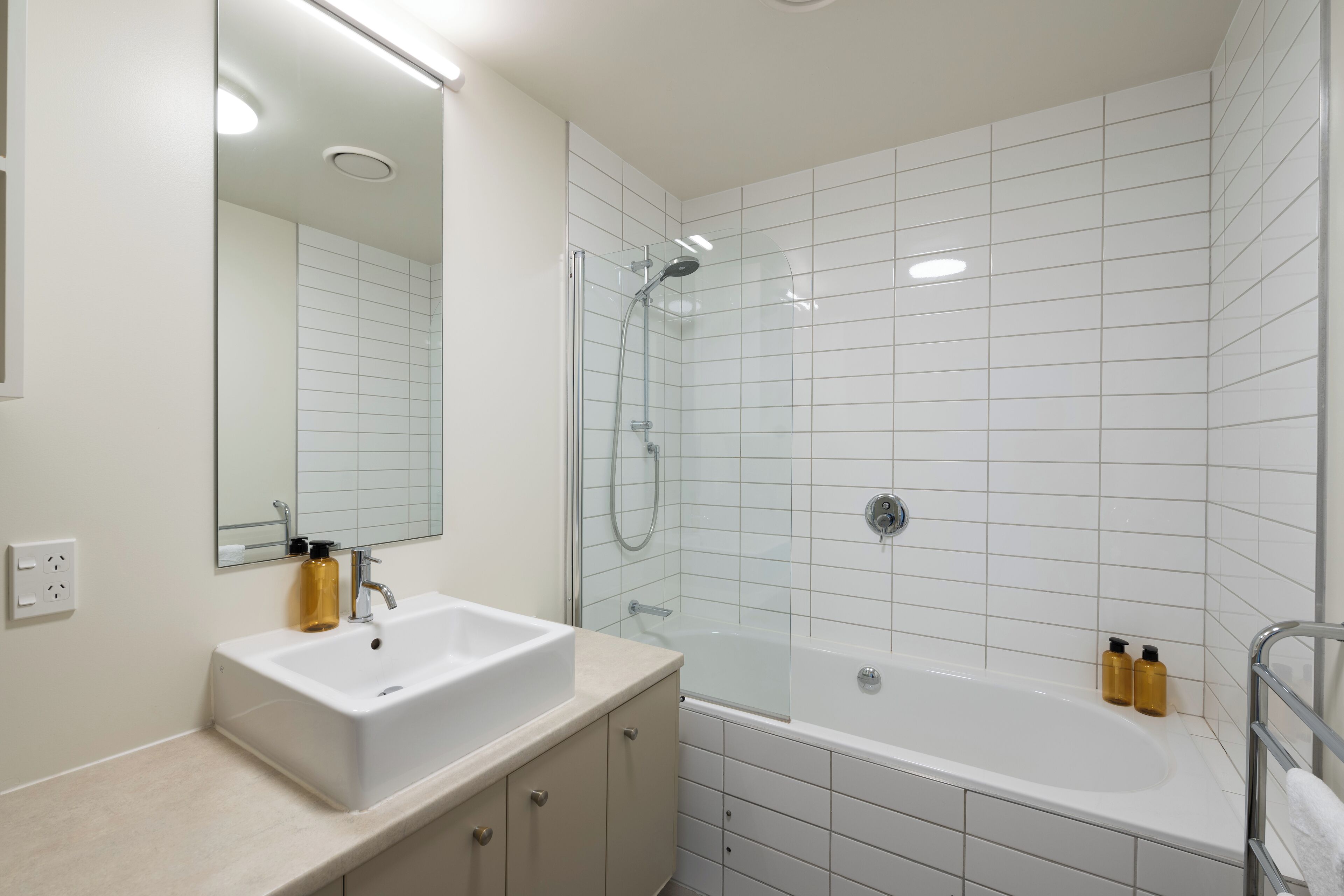 A modern bathroom with a white sink, mirror, and bathtub.