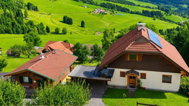 A house with a sloped roof, solar panels, and a view of green fields and mountains.