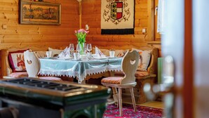 A wooden cabin interior with a dining table set for two, a sofa, and a decorative rug.
