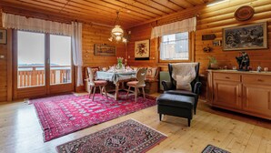 A cozy cabin interior with a dining area, a fireplace, and a view through large windows.