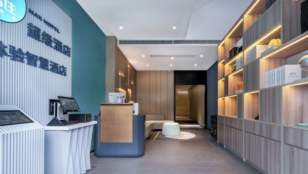 Een moderne hotelreceptie met een receptiebalie, een zithoek en een wand met planken waarop verschillende objecten staan.